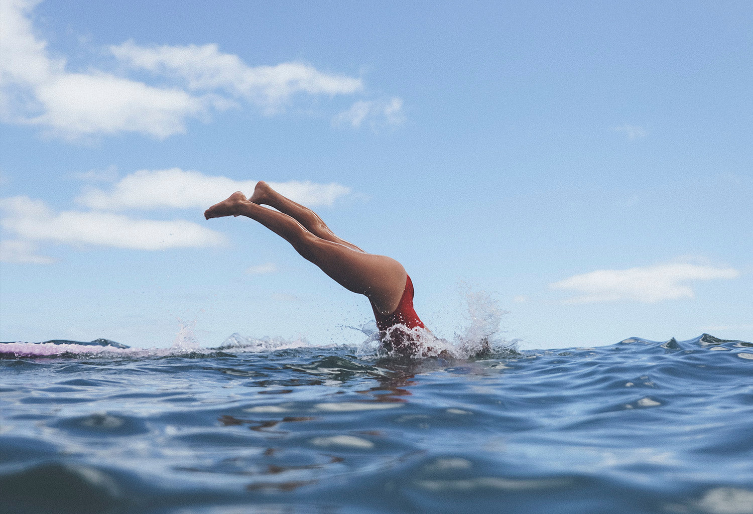 Elise diving into the ocean from her longboard