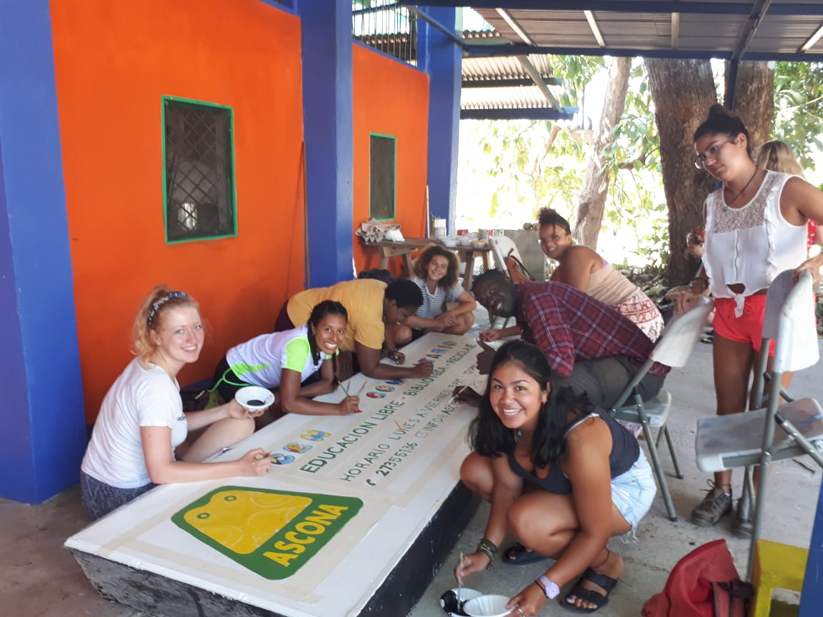 Group of people painting the sign for the Ascona community center and library in Puerto Jimenez