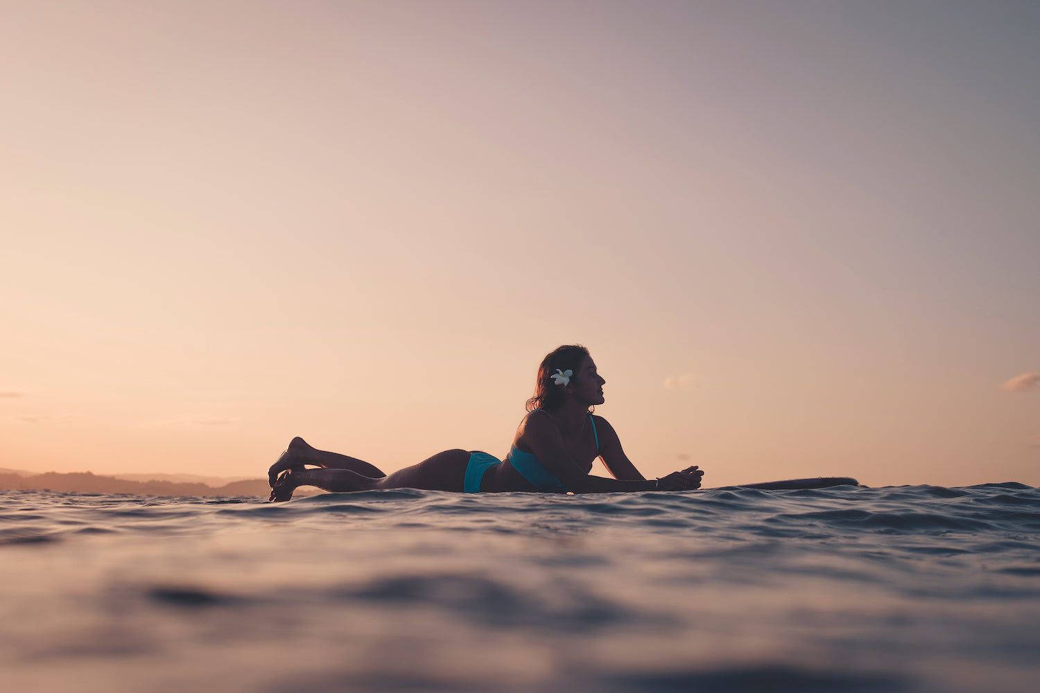 Marie Moana surfing at sunset wearing Dkoko sustainable surf bikinis