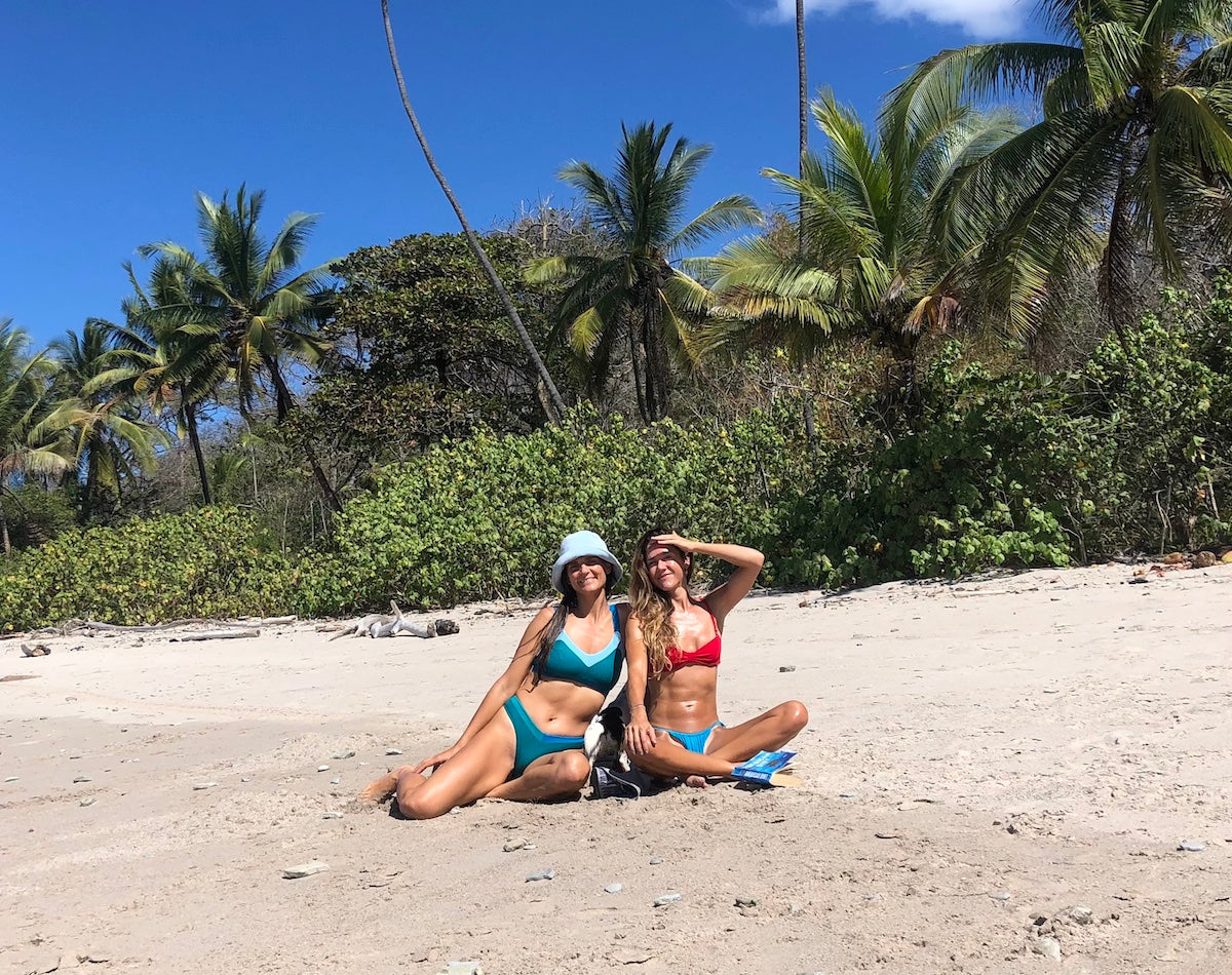 Vero and Mich founders of Dkoko sitting on the sand, wearing their Dkoko bikinis, in Santa Teresa Costa Rica.